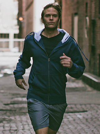 Athlete jogging down an urban alleyway while wearing a Filium-activated, navy hoodie made by Ably
