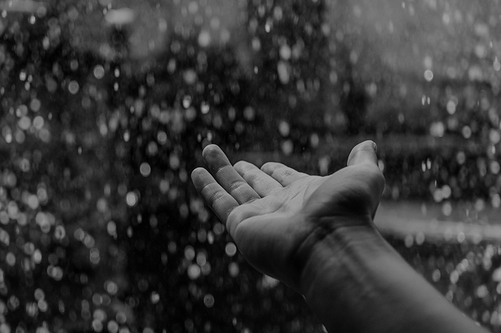 Black and white photo of an outstretched hand in a rain storm