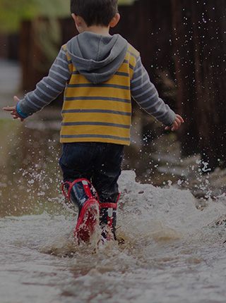 Child splashing in a puddle while wearing Filium-activated clothing [Mobile crop]