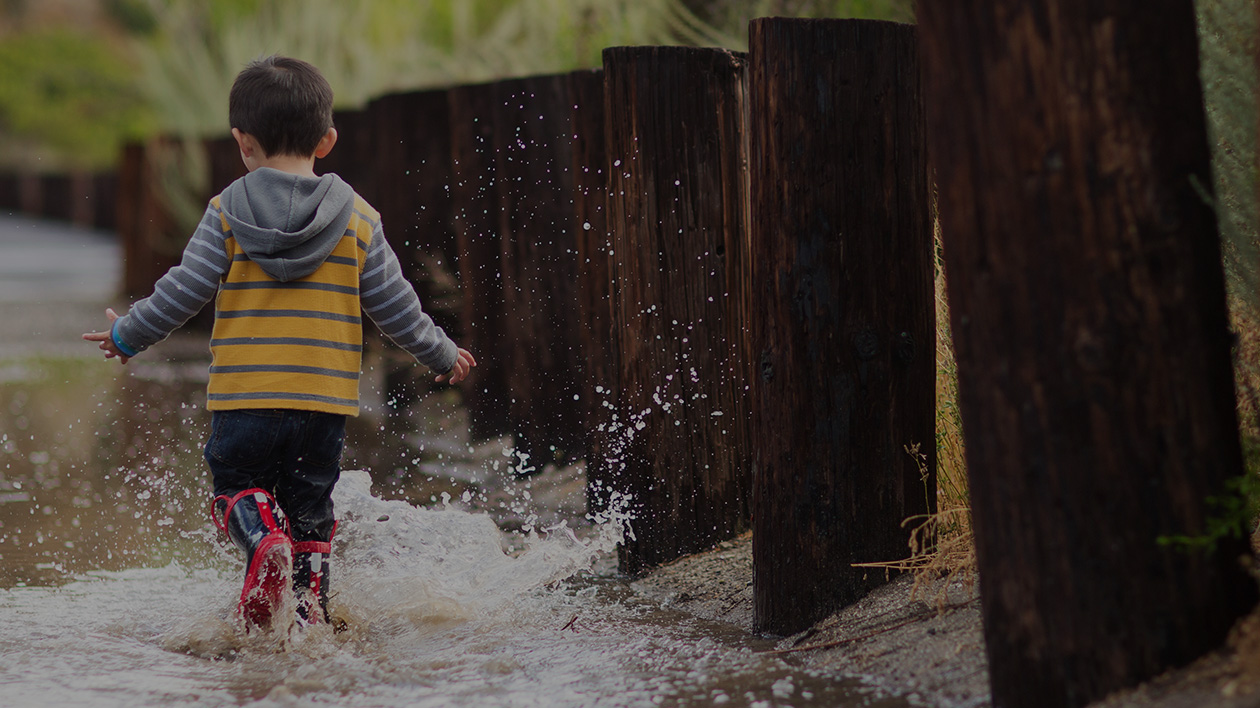 Child splashing in a puddle while wearing Filium-activated clothing