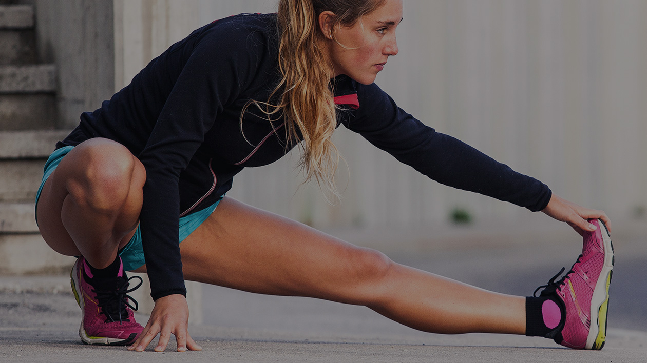 Woman athlete with pink shoes stretches with a serious expression, wearing Filium-activated sports apparel