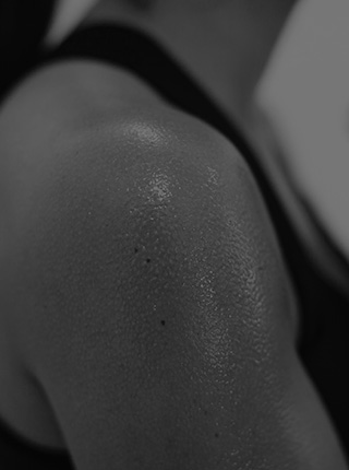 Black and white photo of a bicep of a woman athlete covered in sweat during a workout [Mobile crop]