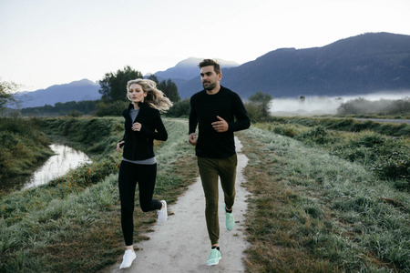 Man and woman wearing Zenkai Sports Apparel Running along a trail by a lake with mountains in the background